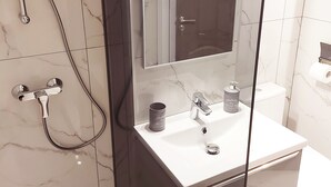 Moderni kylpyhuone, jossa on lasiseinällä varustettu suihku, valkoinen pesuallas ja wc.