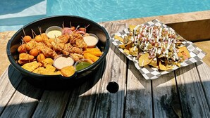 Et bord ved poolen med en skål stegt kylling og en bakke nachos.