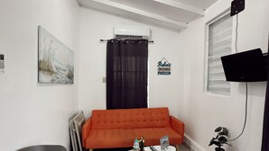 En kompakt opholdsstue med sofa, lille bord, stol, fjernsyn og loftventilator.