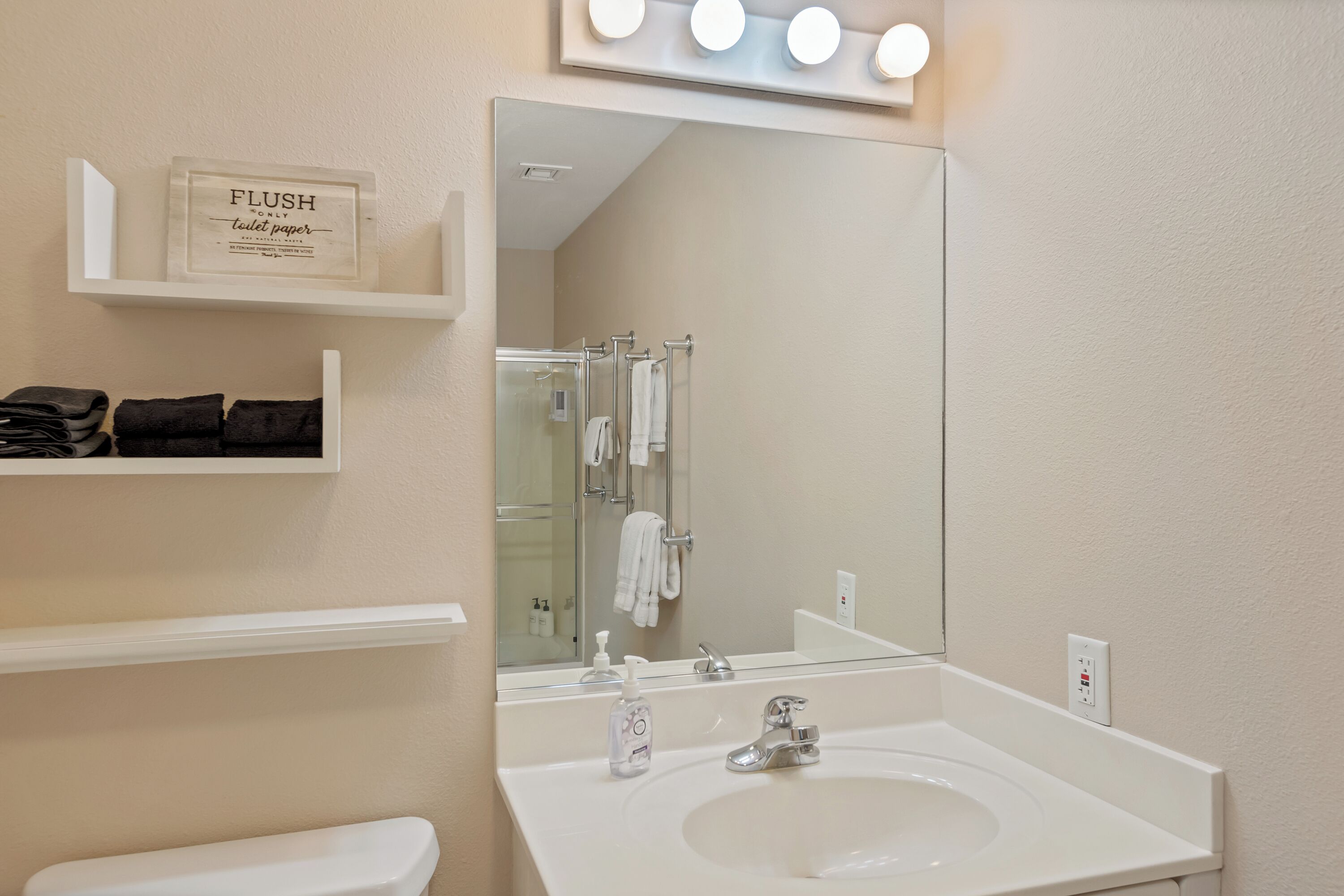 Un baño con lavamanos blanco, un espejo y un estante con artículos de aseo.