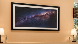 Une chambre d’hôtel avec une grande image de galaxie encadrée au mur, un lit avec une literie blanche et deux tables de chevet avec des lampes et de petites plantes.