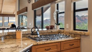 Une cuisine dotée de plans de travail en granit, d’une cuisinière à gaz et de grandes fenêtres offrant une vue sur les montagnes.