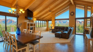 Un salon spacieux avec une grande table à manger, des sièges confortables et une vue sur les montagnes grâce à de grandes fenêtres.