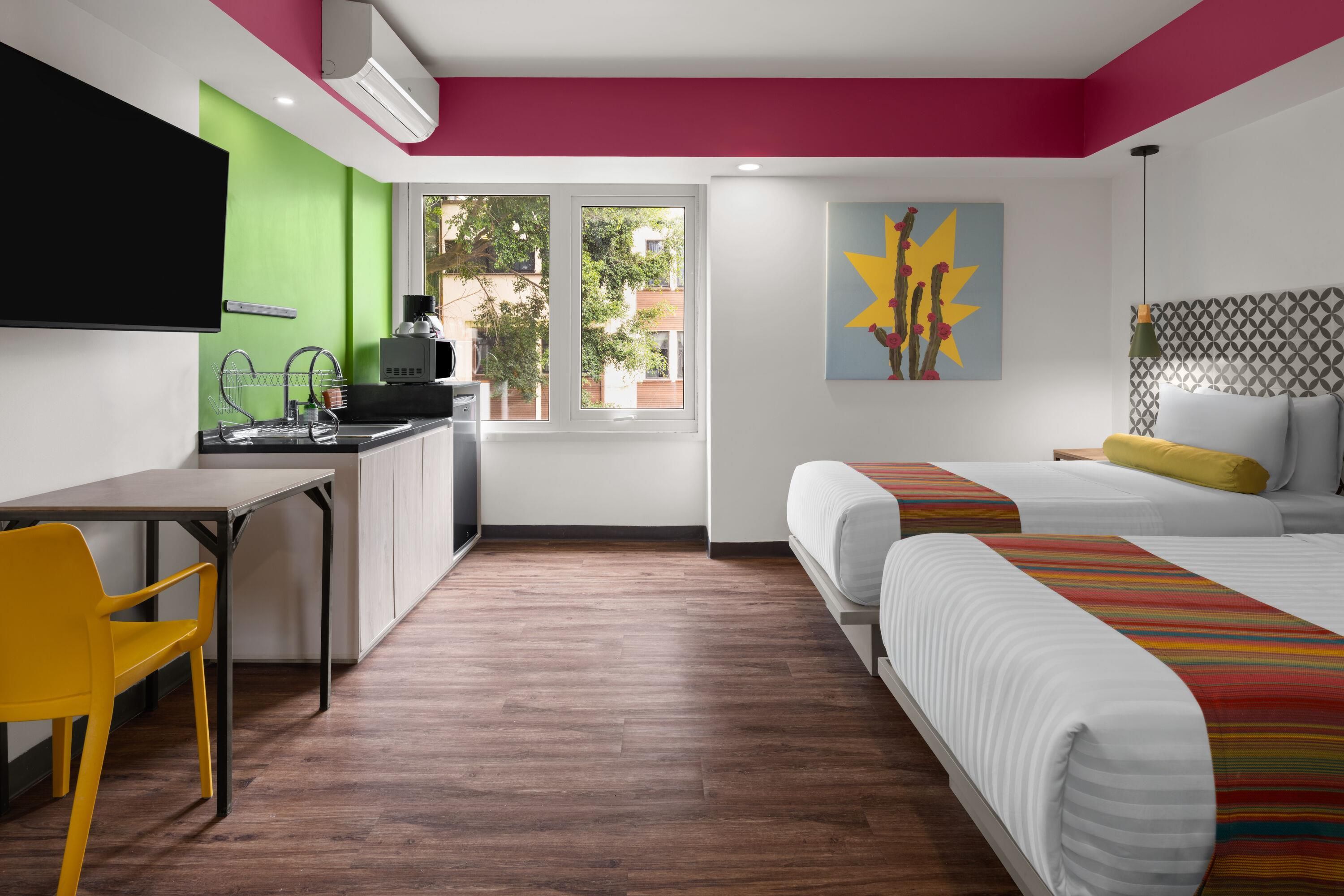 Habitación de hotel con escritorio, una silla, cama, ventana y un cuadro en la pared.