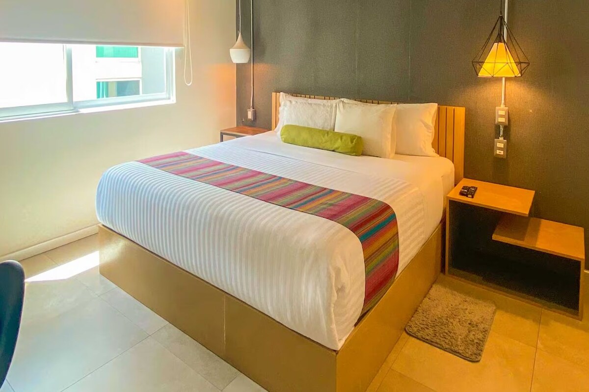 A hotel room with a bed, bedside tables, a lamp, a chair, and a window.