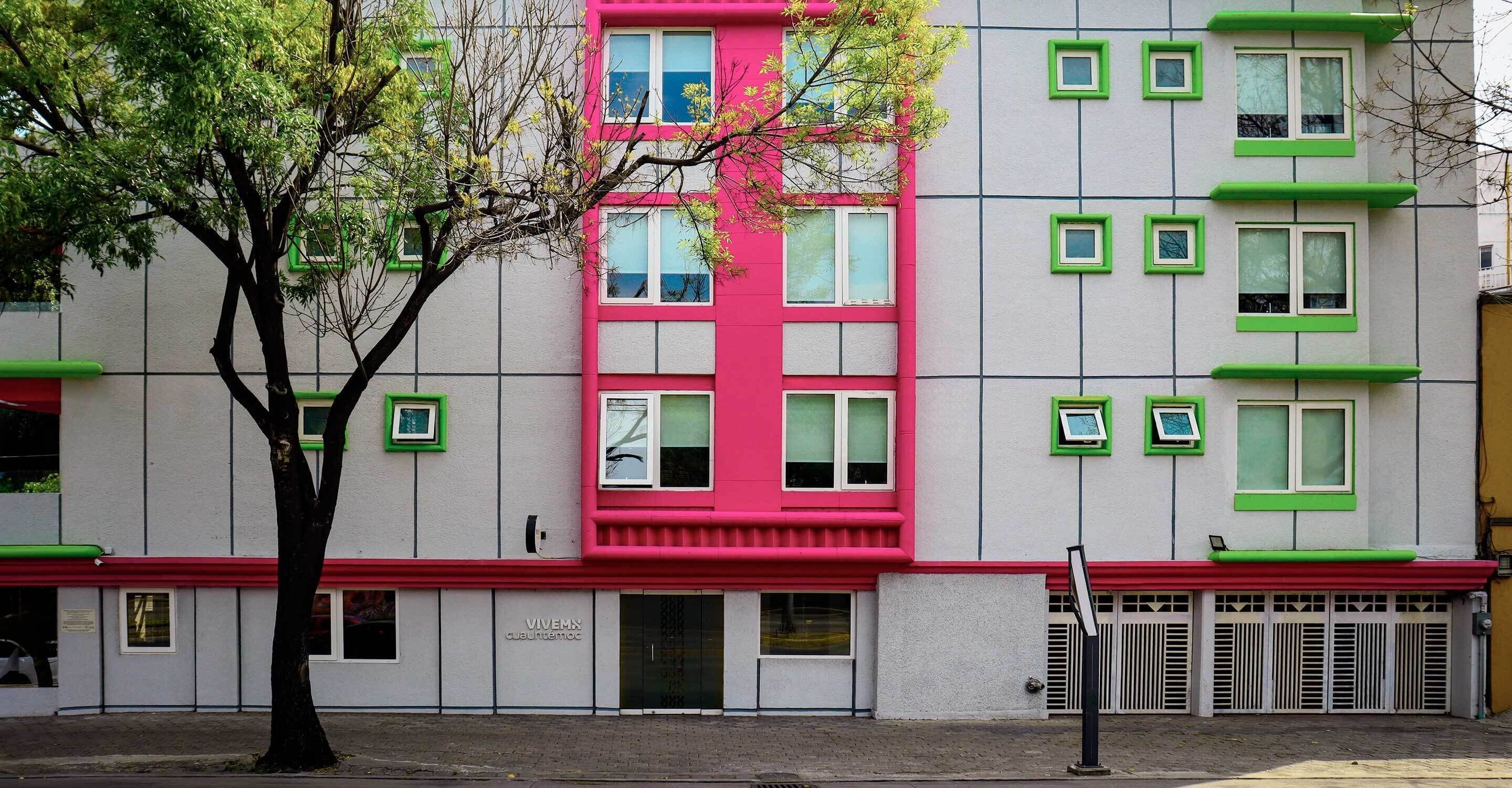 A multi-story building with a distinctive pink and green facade, featuring a series of windows and a visible entrance.