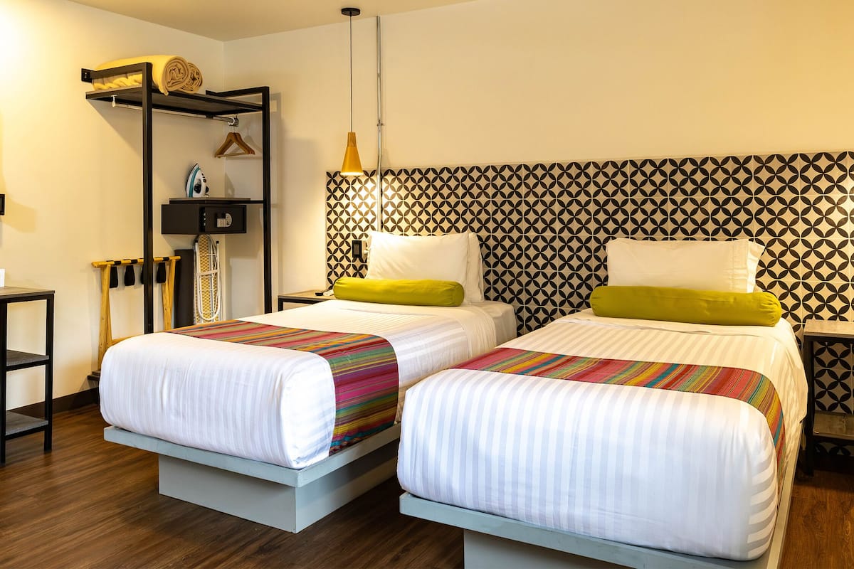 Une chambre d’hôtel avec deux lits, une armoire, un bureau et un mur décoré d’un motif.
