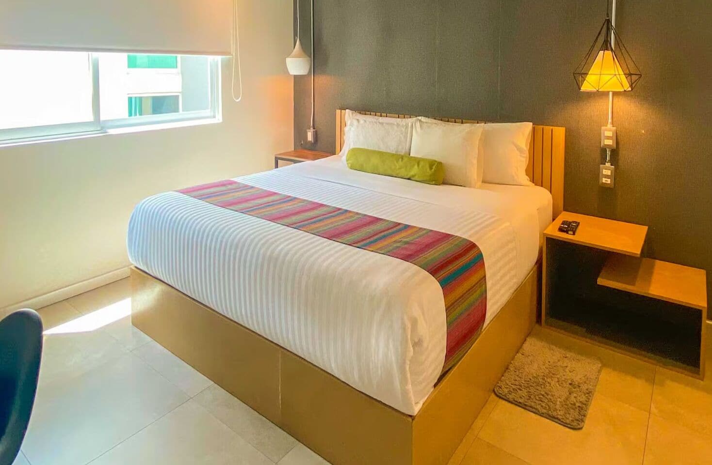 A hotel room with a bed, bedside tables, a lamp, a chair, and a window.