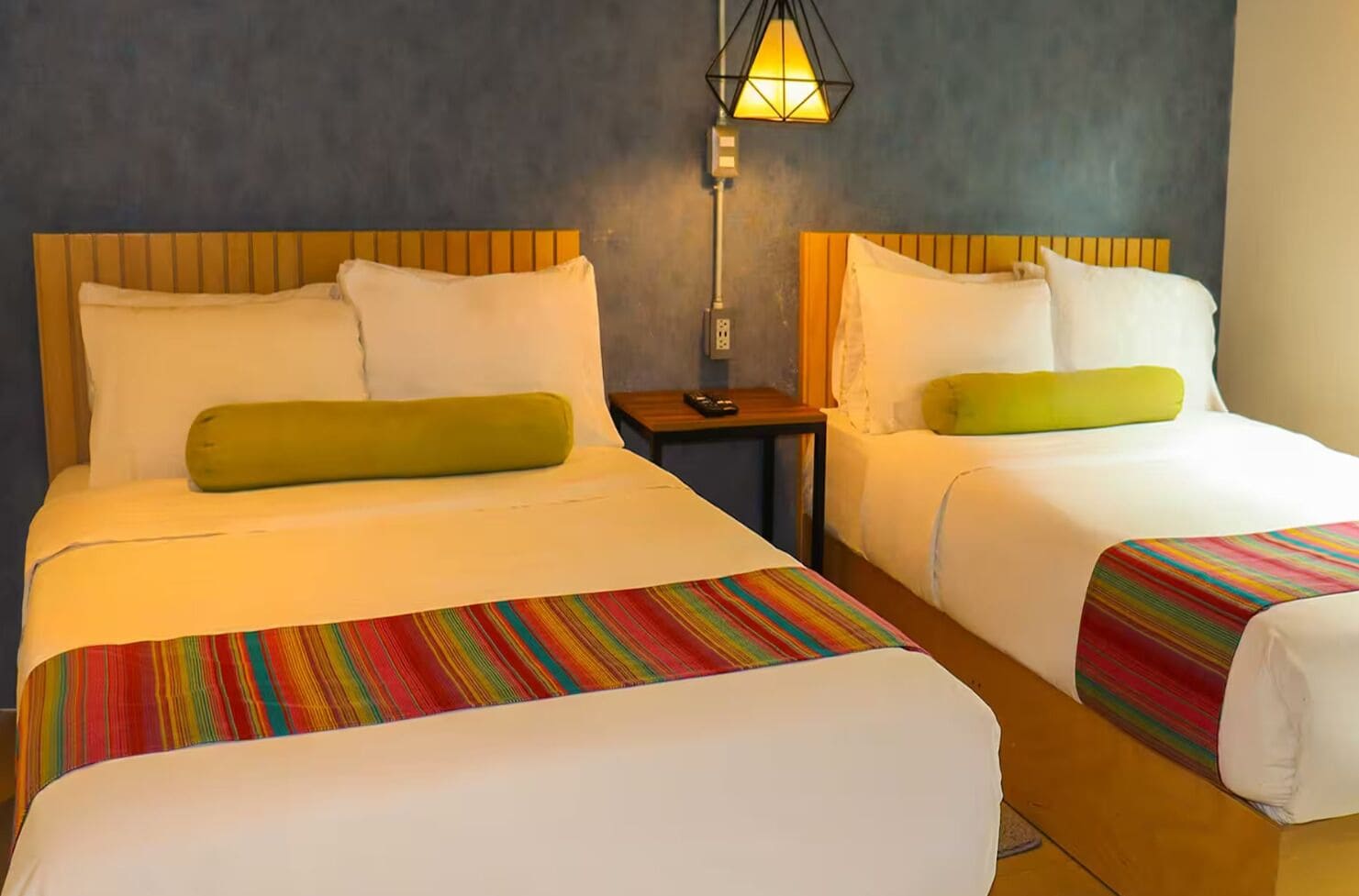 Two beds with wooden headboards, white bedding, and colorful striped bedspreads.