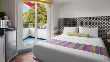A hotel room with a bed, a desk, a microwave, and a view of a balcony with a pool.