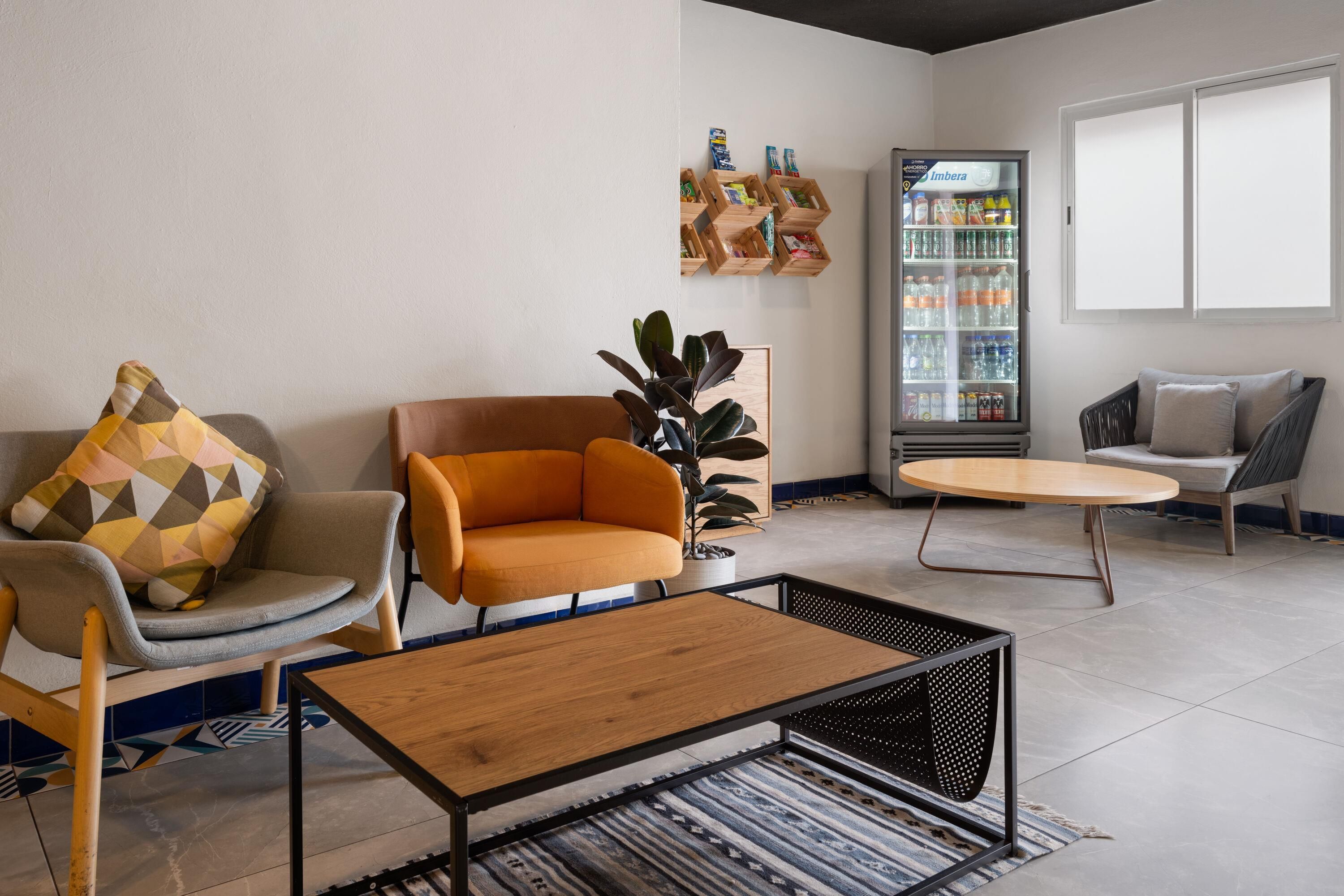 Un espace détente moderne comprenant des sièges, une table basse, une plante et un réfrigérateur pour boissons.