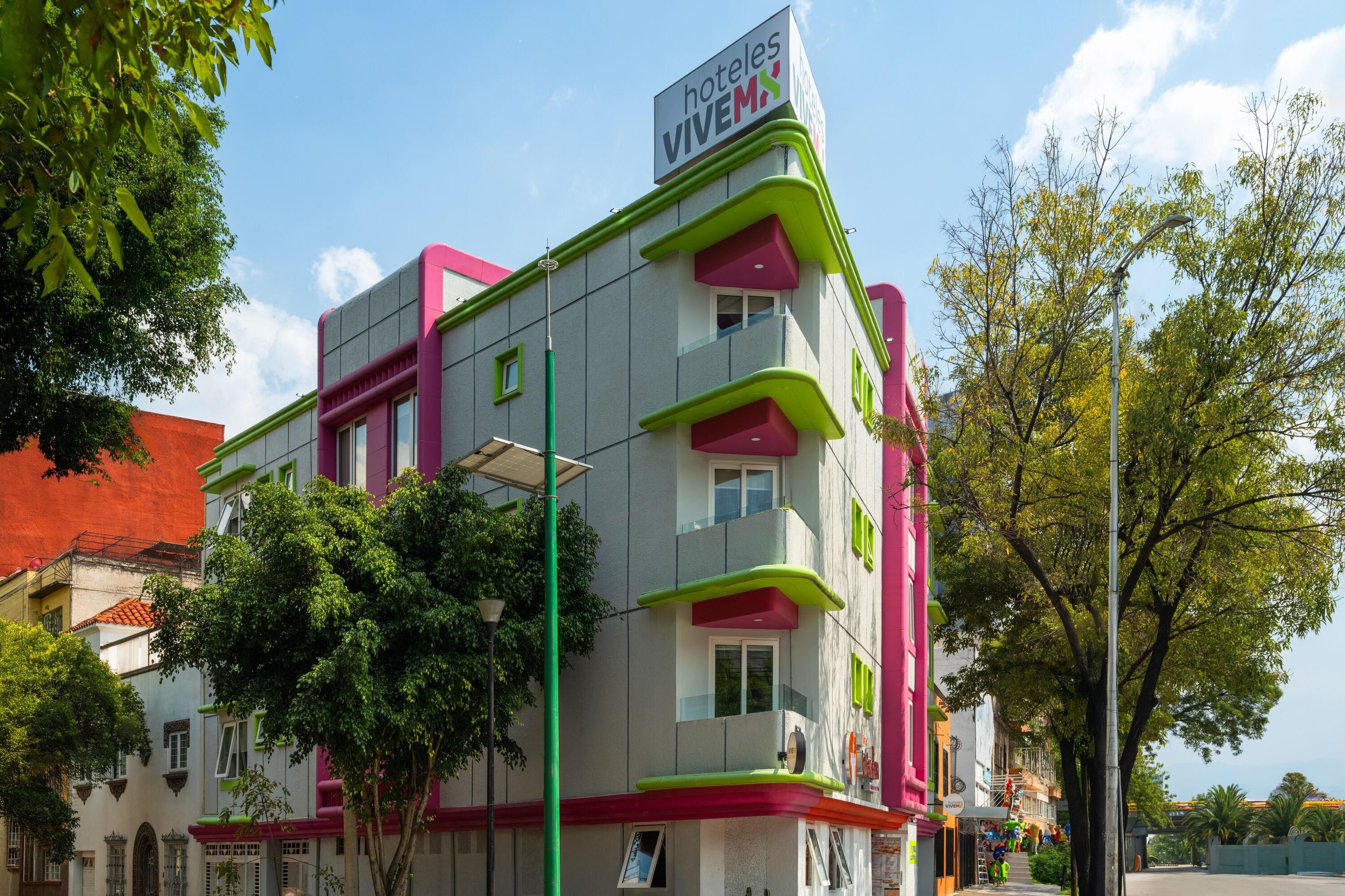 Ein mehrstöckiges Hotel mit einer auffälligen rosa-grünen Fassade, einem Schild, das es als Hotel kennzeichnet, und freiem Blick auf die umliegende Stadt.