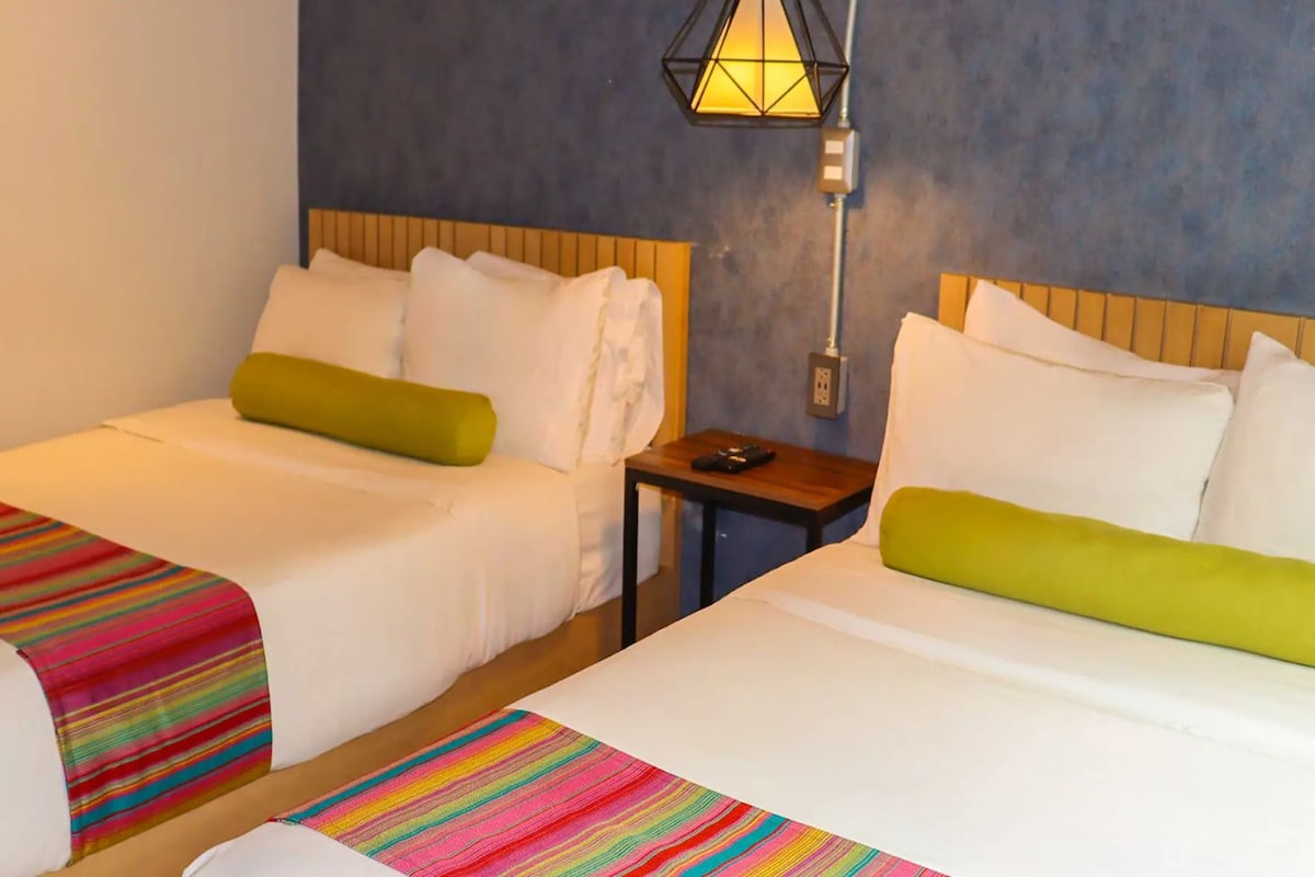 Habitación de hotel con dos camas, una mesita de noche, una lámpara y una alfombra a rayas.