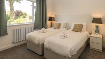 Habitación doble con dos camas, una ventana con cortinas, una mesita de noche con lámpara y un radiador.