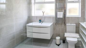 A modern bathroom with a white sink, toilet, and a window with a view.