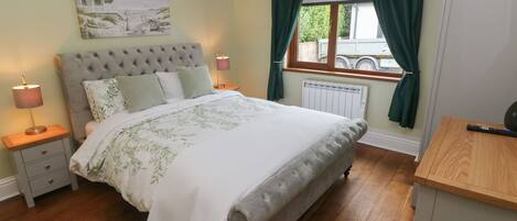 A neatly arranged bedroom with a large bed, bedside lamps, a radiator, and a window with curtains.