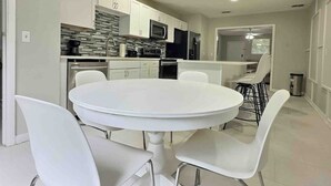 A modern kitchen with white cabinets, a round dining table, and white chairs.