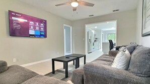 Een moderne woonkamer met een flatscreen televisie aan de muur, een plafondventilator en een bank met kussens.
