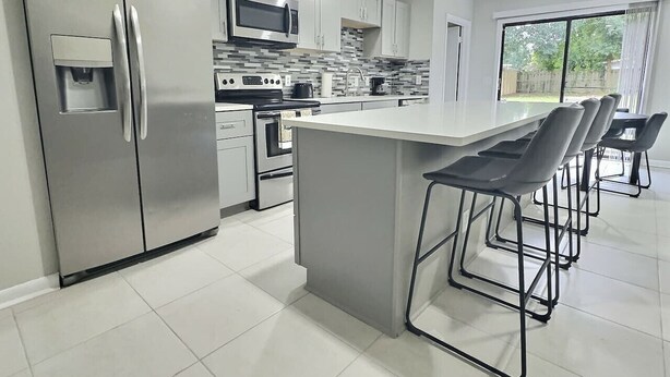 Een moderne keuken met roestvrijstalen apparatuur, een centraal eiland met barkrukken, en een groot raam met uitzicht op de omgeving.