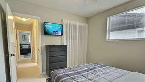 Een slaapkamer met een bed, een kaptafel, een televisie aan de muur en een raam met jaloezieën.