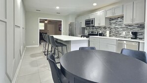Een moderne keuken met witte kasten, een centraal eiland en een eetgedeelte met een ronde tafel en stoelen.