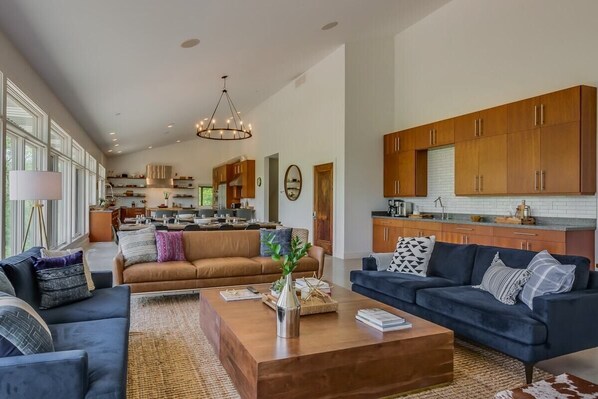 A spacious living room with a large sofa, a coffee table, and a dining area with wooden cabinets and a kitchen in the background.