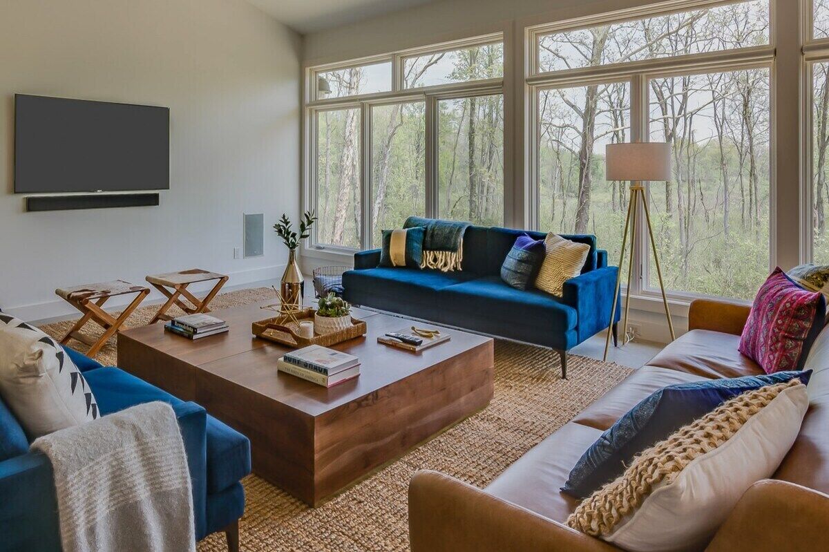 A modern living room with a blue sofa, a wooden coffee table, and a large window with a view of trees.
