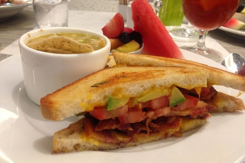 A grilled cheese sandwich with tomato, bacon, and avocado on a white plate.