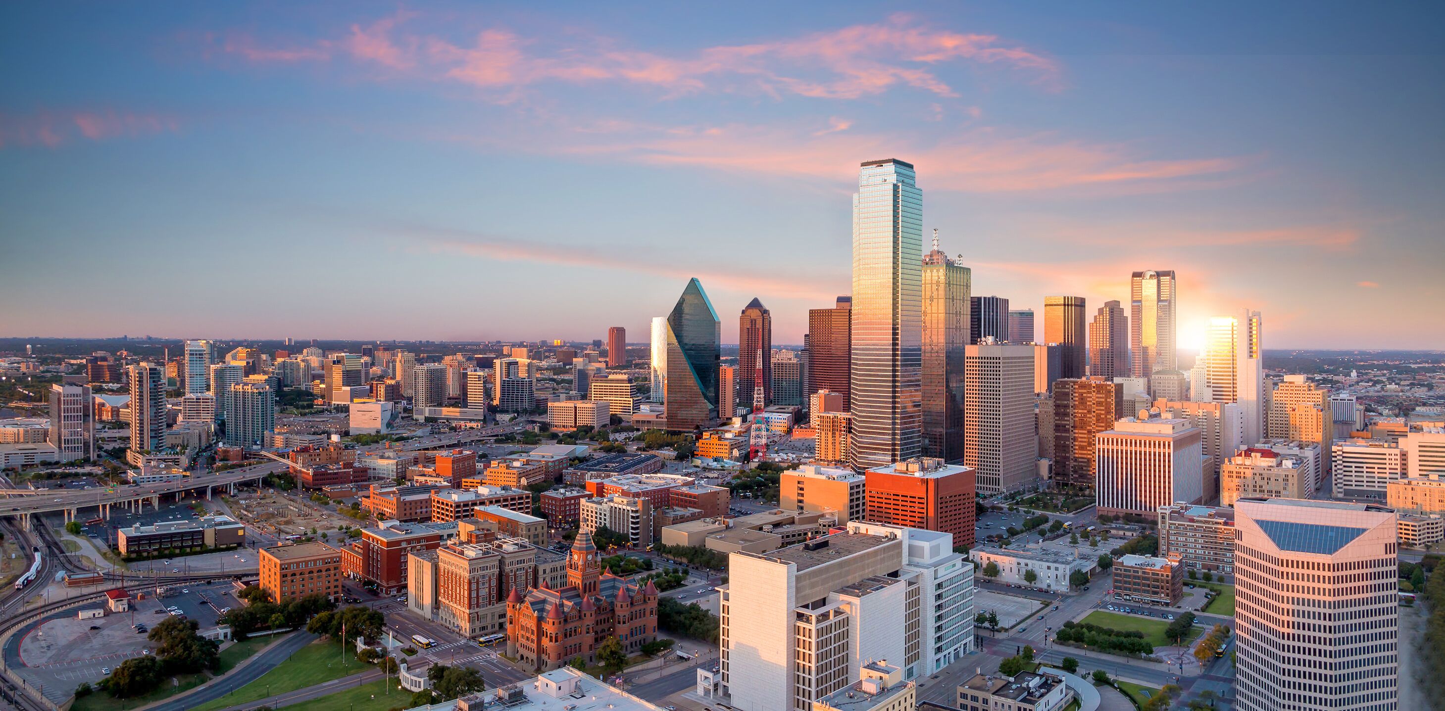 A cityscape with a prominent skyscraper, a mix of modern and older buildings, and a clear sky.