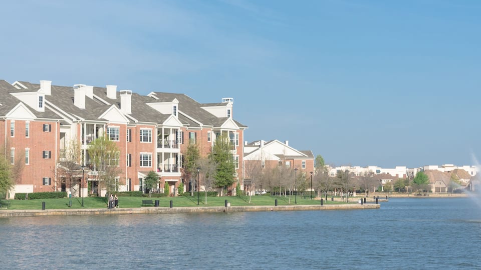 A waterfront with a row of brick buildings, a fountain, and a clear sky.
