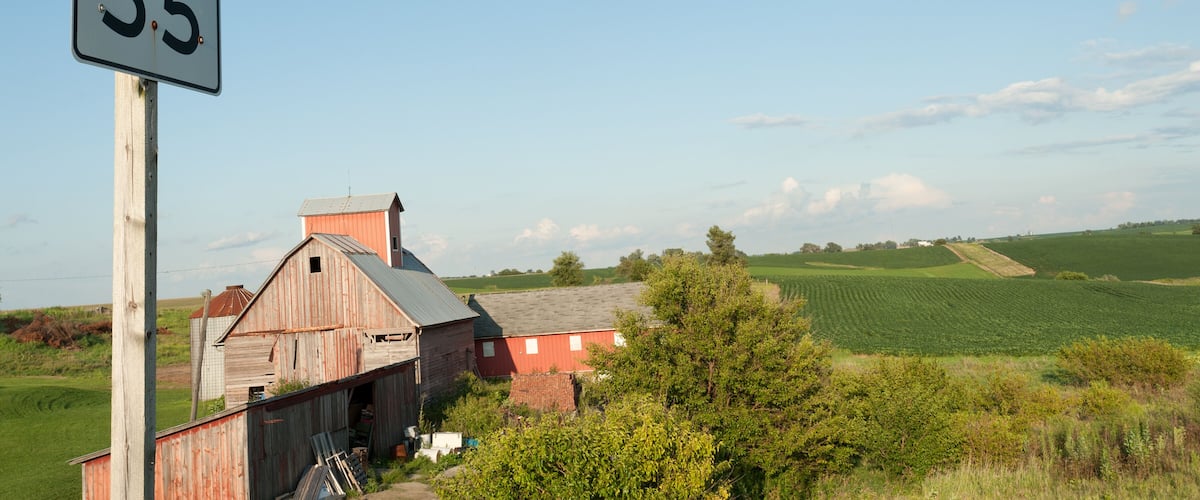 A rural landscape with a barn, a speed limit sign, and expansive fields.