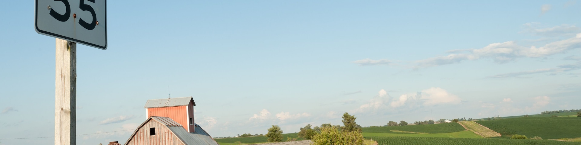 A rural landscape with a barn, a speed limit sign, and expansive fields.