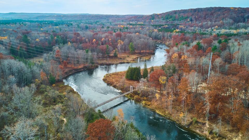 A river winding through a forest with a bridge and power lines.
