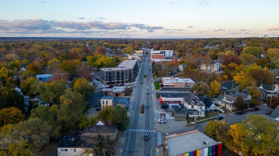 An aerial view of a town with autumn-colored trees, a central road, and various buildings.