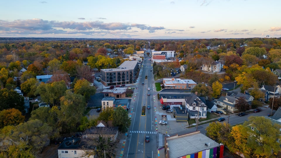 An aerial view of a town with autumn-colored trees, a central road, and various buildings.
