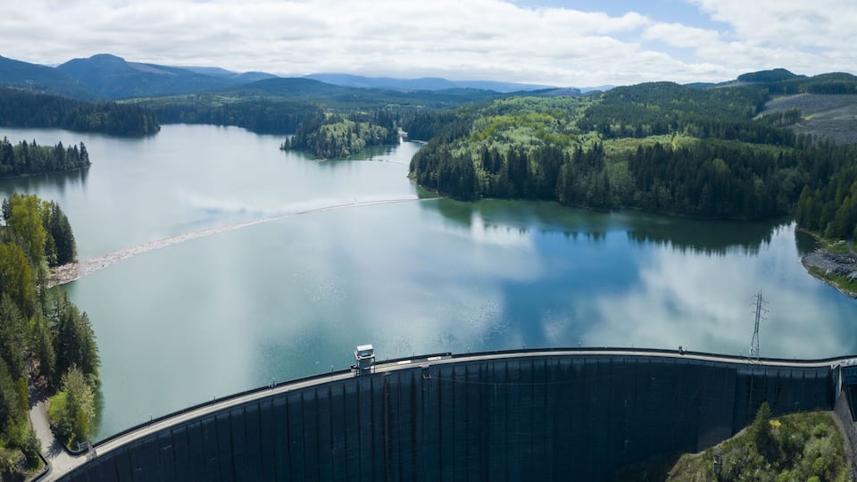 A large dam with a reservoir and surrounding forested hills.