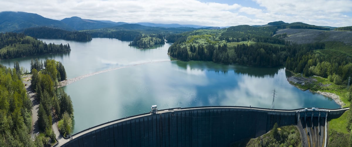 A large dam with a reservoir and surrounding forested hills.