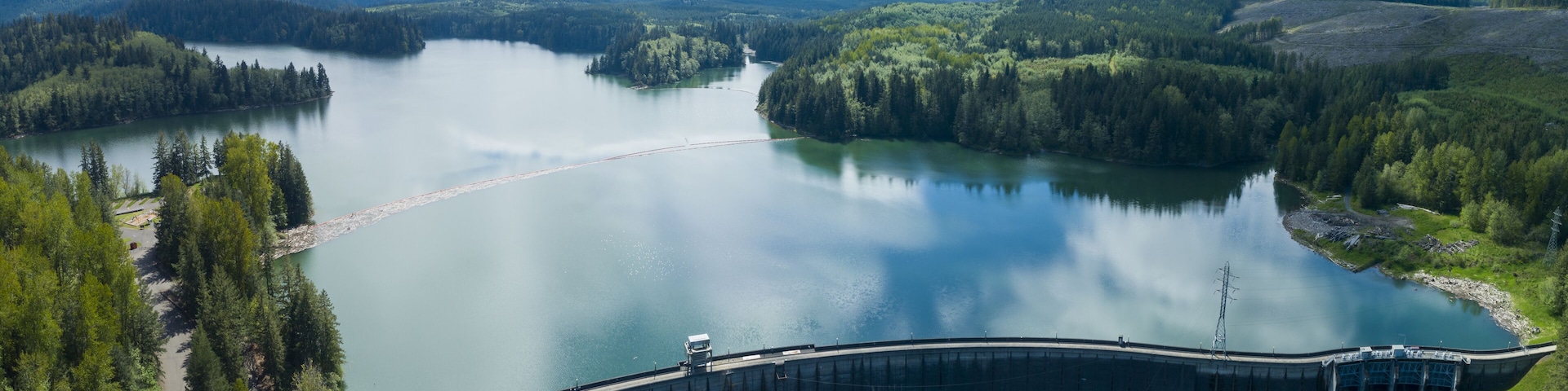 A large dam with a reservoir and surrounding forested hills.