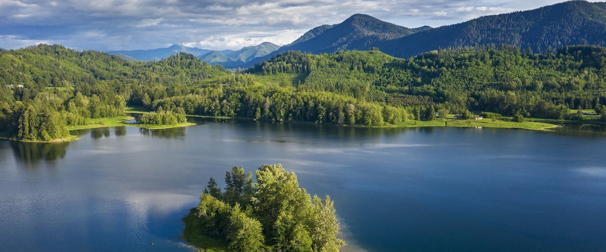 A serene lake surrounded by lush green hills and mountains under a partly cloudy sky.