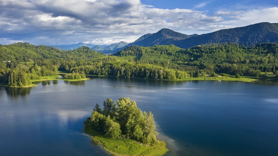 A serene lake surrounded by lush green hills and mountains under a partly cloudy sky.