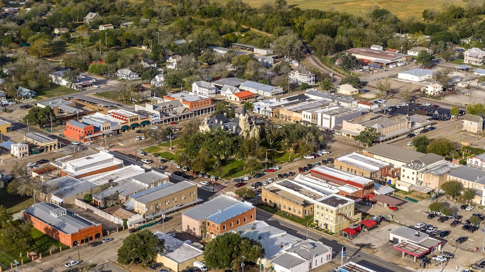 An aerial view of a small town with a mix of residential and commercial buildings, a central church, and a main road.