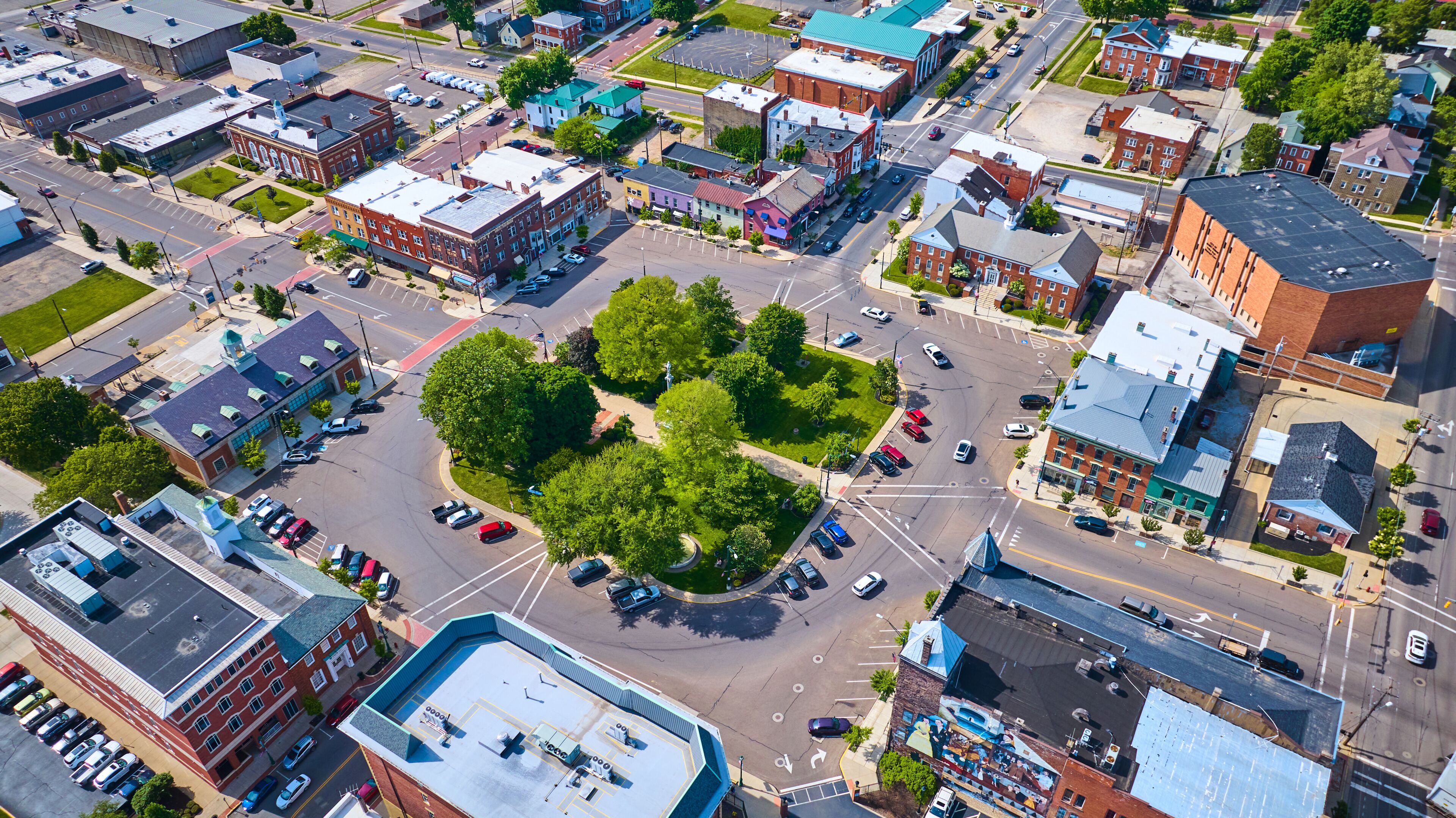 An aerial view of a city intersection with surrounding buildings, roads, and a central green space.