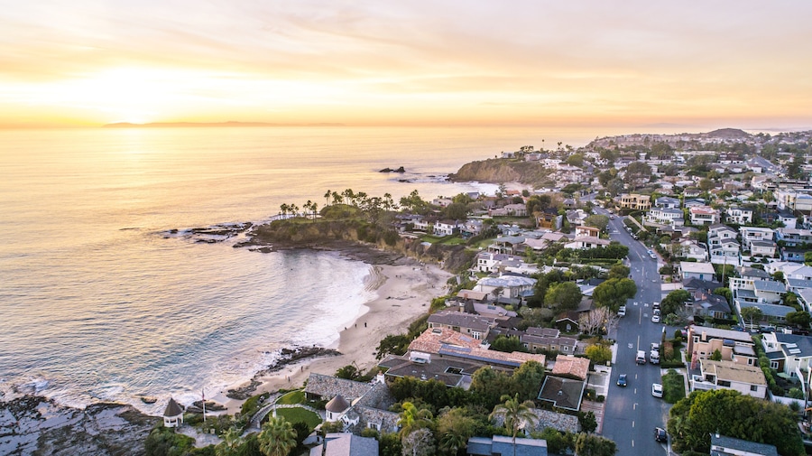 A coastal town with a beach, houses, and a sunset over the ocean.