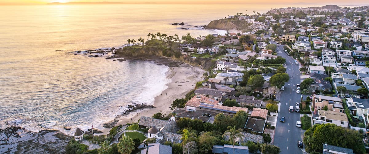 A coastal town with a beach, houses, and a sunset over the ocean.