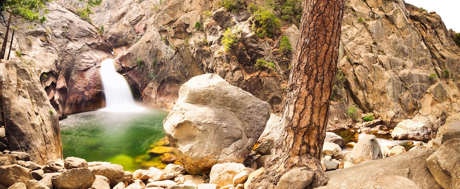 A waterfall cascading into a pool surrounded by rocky terrain and sparse vegetation.
