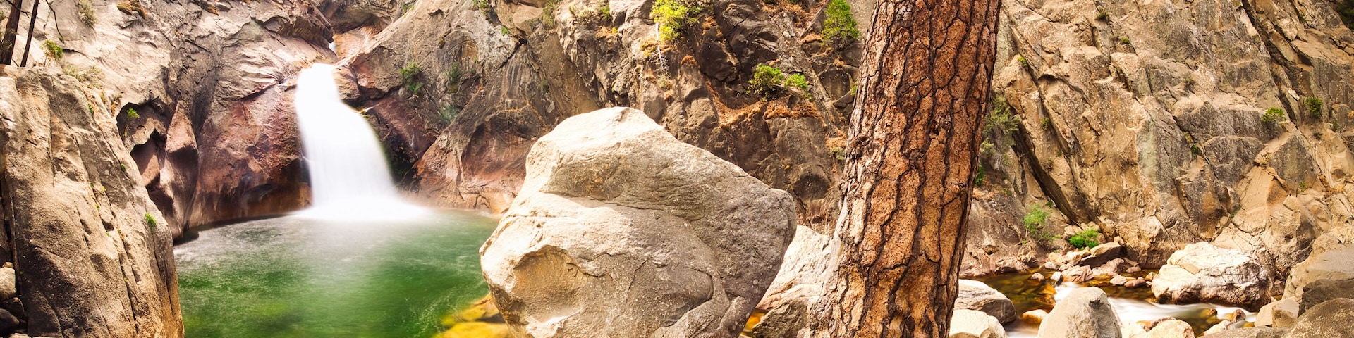 A waterfall cascading into a pool surrounded by rocky terrain and sparse vegetation.
