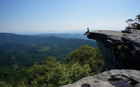A person sitting on a rock ledge overlooking a forested valley.