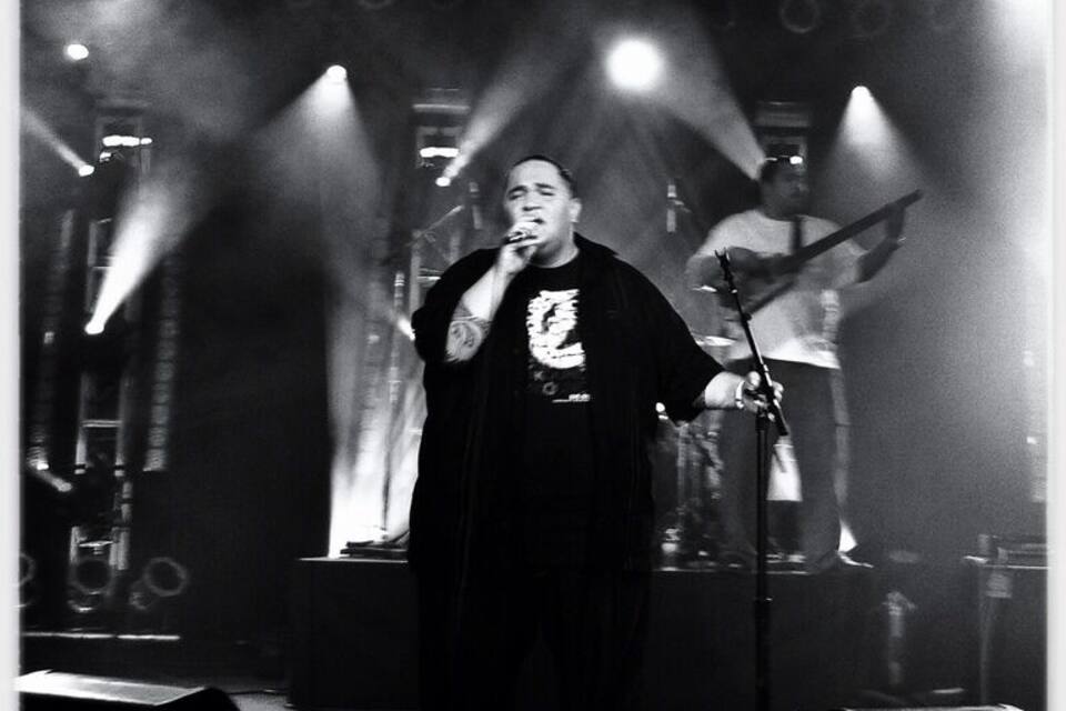 Una persona canta sul palco mentre, sullo sfondo, un chitarrista suona.