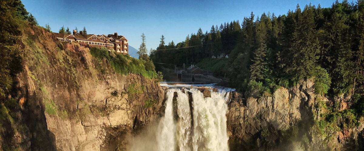 A waterfall cascading down a rocky cliff, surrounded by lush greenery and a large building on the cliffside.