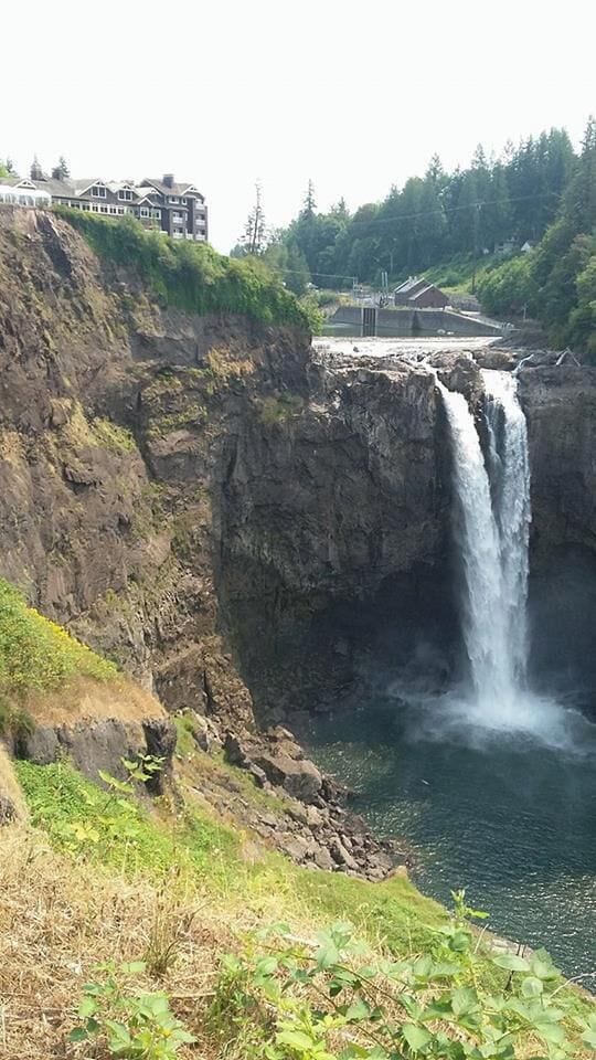 A waterfall cascading down a rocky cliff into a body of water, with buildings in the background.